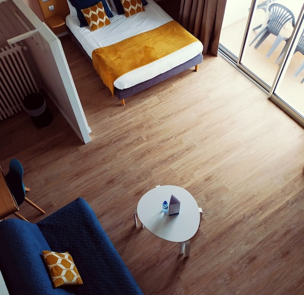 A hotel room with a bed, a small round table with a water bottle and wallet, a chair, and a view of outdoor chairs through a glass door. - Brit Hotel Hermitage (Royan)