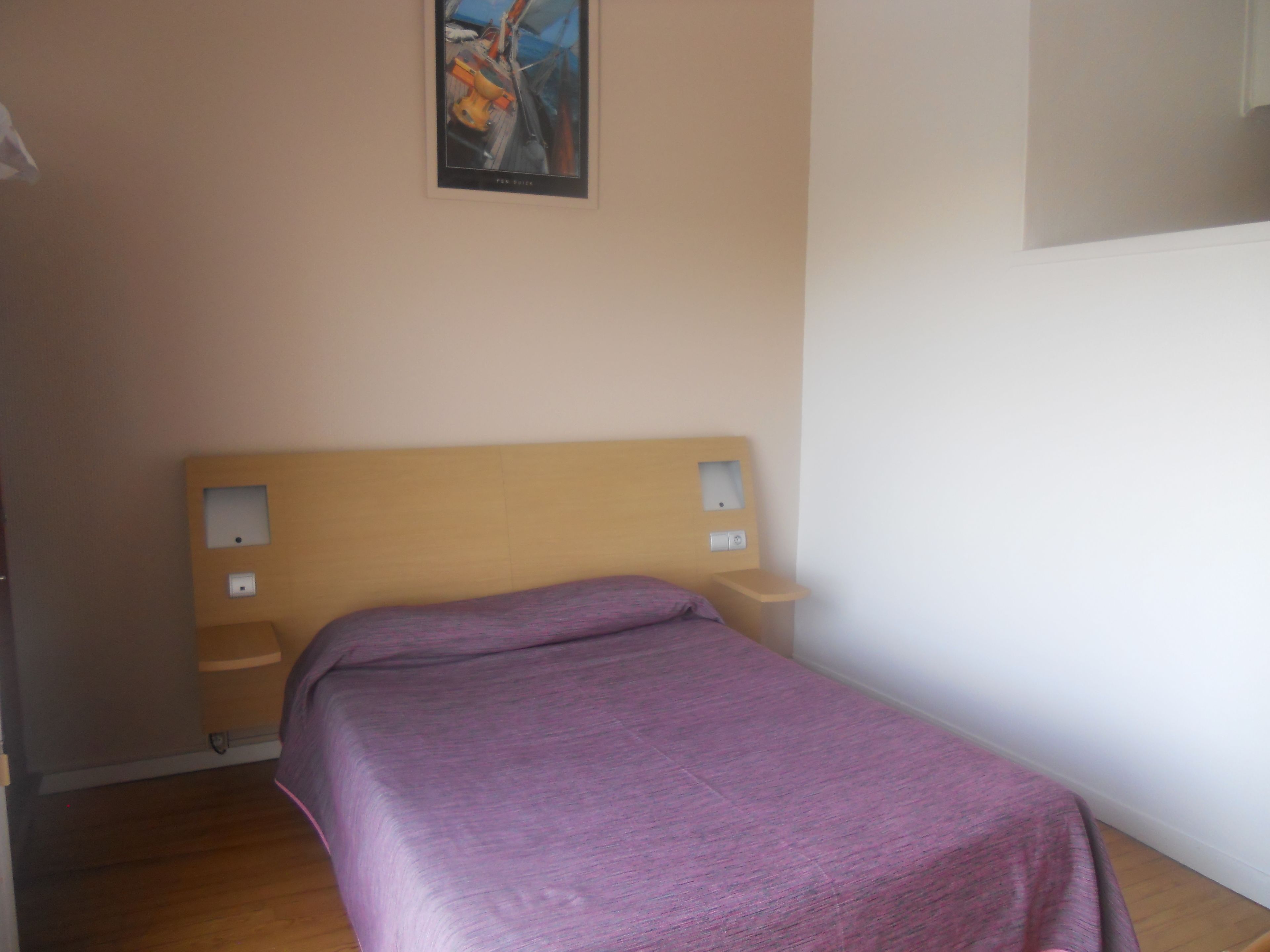 A small, simple bedroom with a single bed, a wooden headboard, and two bedside tables.