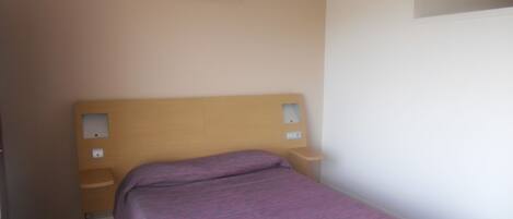 A small, simple bedroom with a single bed, a wooden headboard, and two bedside tables.