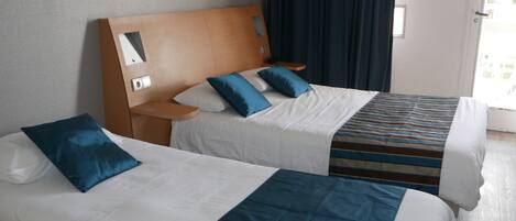 Una habitación de hotel con dos camas, cabecera de madera, mesita de noche y ventana con cortinas.