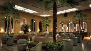 A spacious lobby with seating areas, large potted plants, and a bar with shelves of bottles. - Anantara Palais Hansen Vienna – A Leading Hotel of the World (Vienna)
