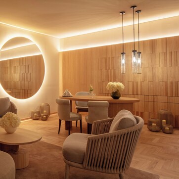 A modern interior with a round mirror, wooden panel walls, and a dining area with chairs and a table.