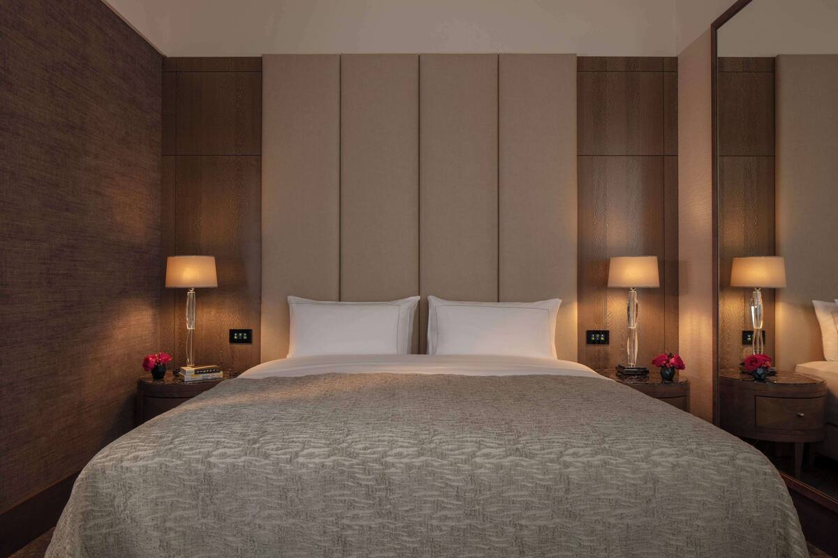 Ein Hotelzimmer mit einem großen Bett, zwei Nachttischen mit Lampen und einem Spiegel an der Wand.