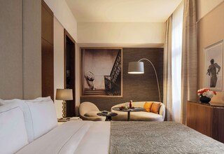 A hotel room with a large bed, a sofa, a small table with a lamp, and a painting on the wall.