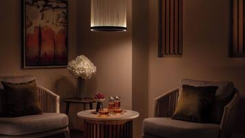 A room with two armchairs, a round wooden table with a vase of flowers, a painting on the wall, and a pendant light.