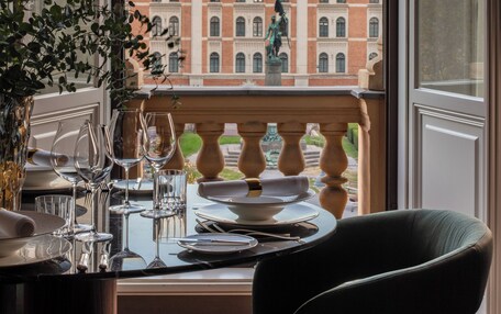 A dining area with a view of a historic building, a balcony with a balustrade, and a table set with wine glasses and plates.