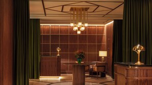 A lobby with a reception desk, a round table with chairs, a vase with flowers, and a lamp.