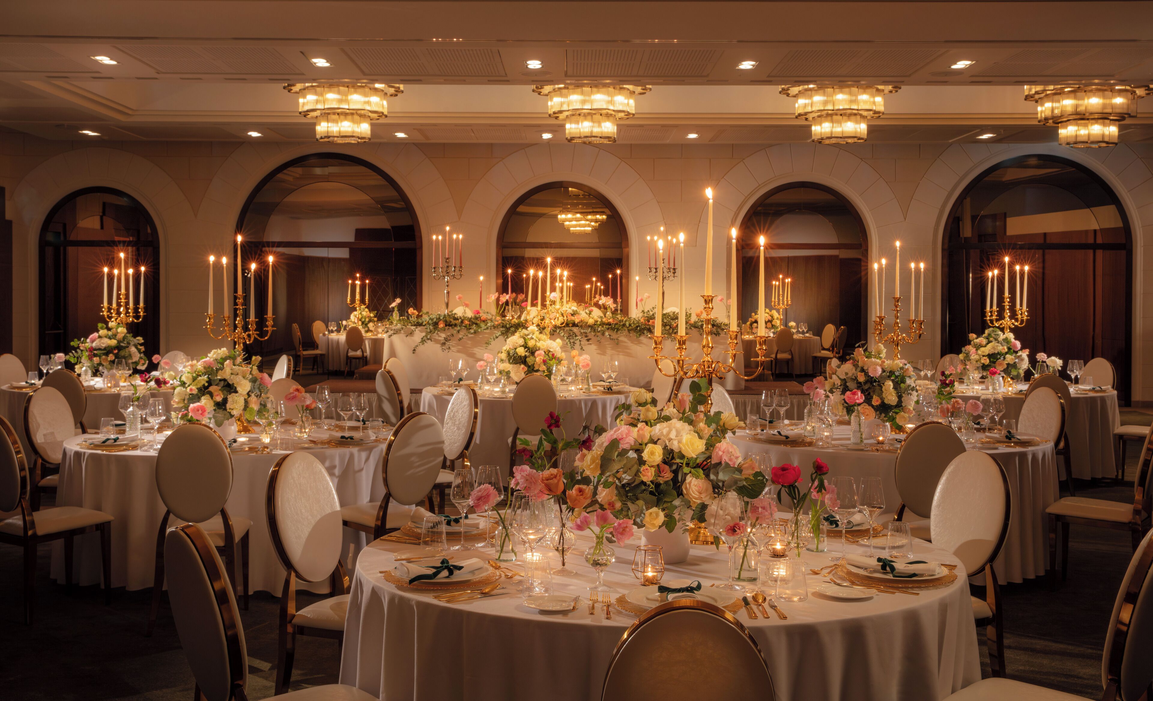 Uma sala de banquetes com mesas redondas, lustres e arranjos florais.