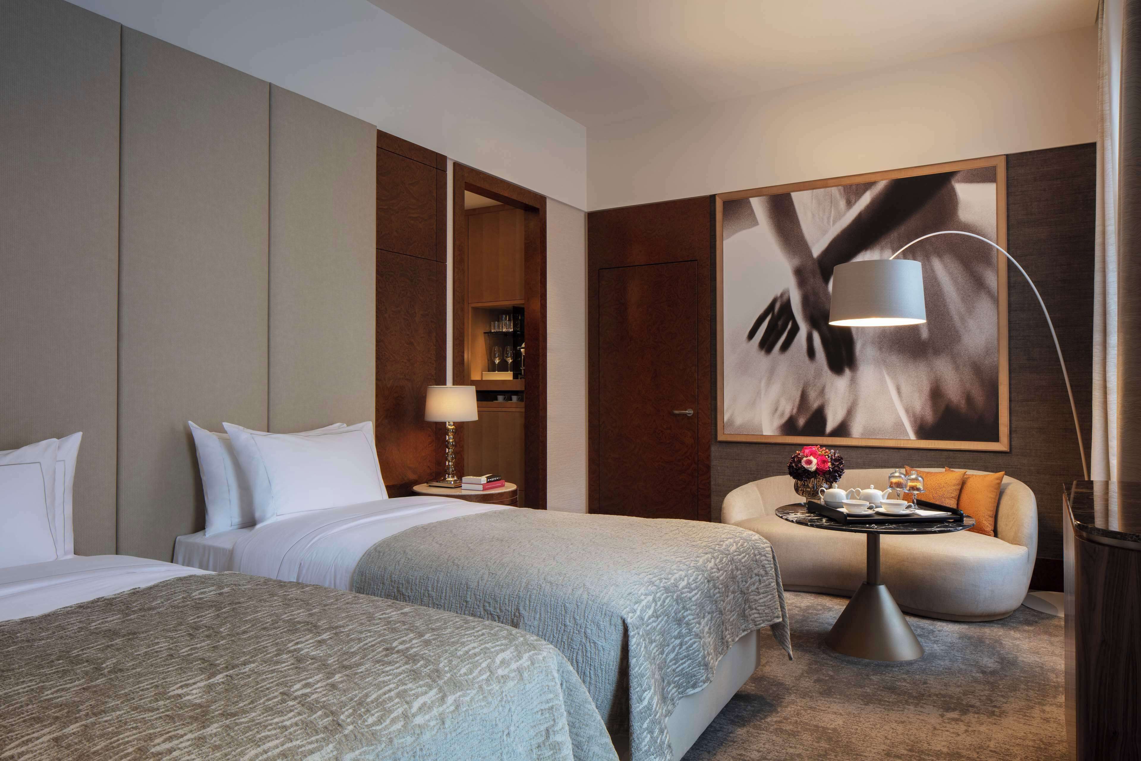 Una habitación de hotel con dos camas, un sofá, una mesa de centro, una lámpara y un cuadro abstracto grande en la pared.