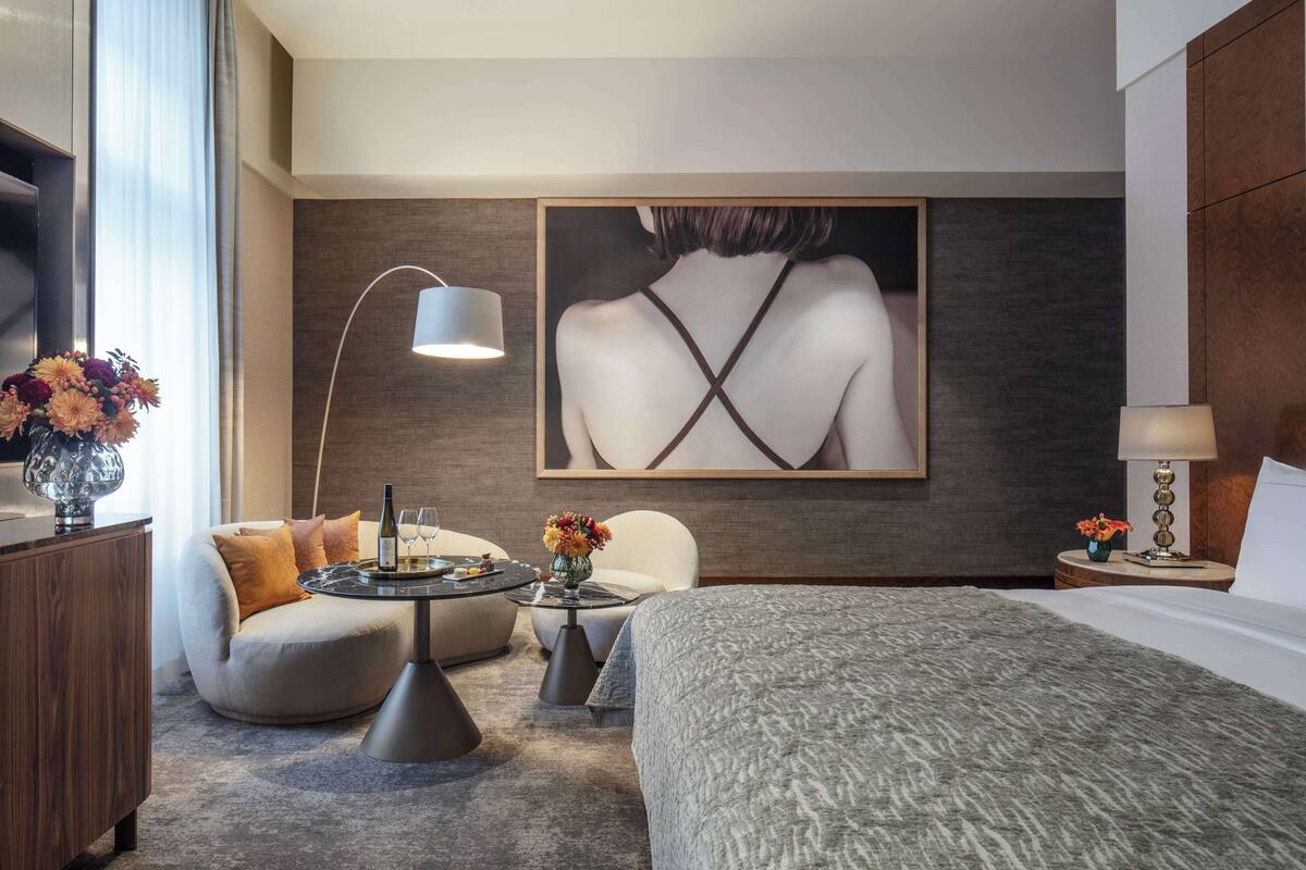 Ein modernes Hotelzimmer mit einem Bett, einem runden Tisch, zwei Sesseln, einem Couchtisch und einem großen Gemälde an der Wand.
