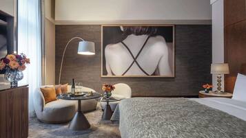 A modern hotel room with a bed, a round table, two armchairs, a coffee table, and a large painting on the wall.