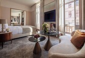 A hotel room with a bed, a sofa, a coffee table, a TV, and a balcony with a view of buildings.