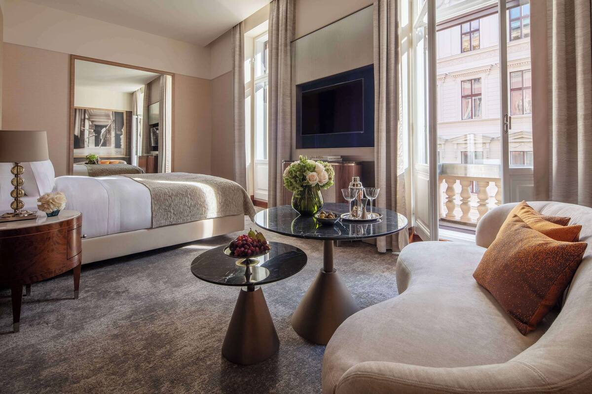 Ein Hotelzimmer mit Bett, einer Couch, einem Couchtisch, einem Fernseher und einem Balkon mit Blick auf Gebäude.