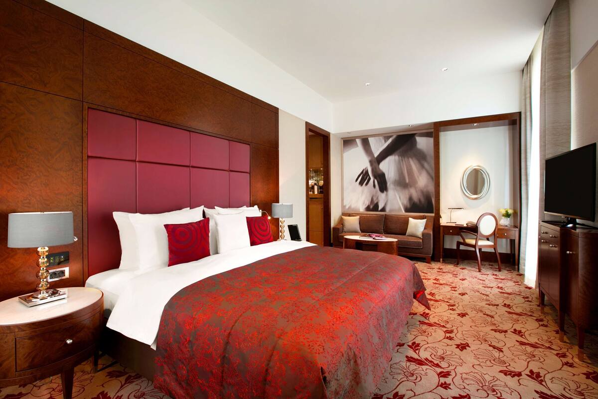 Ein Hotelzimmer mit einem großen Bett, einem Schreibtisch, einem Sessel, einem Fernseher und einem Spiegel.