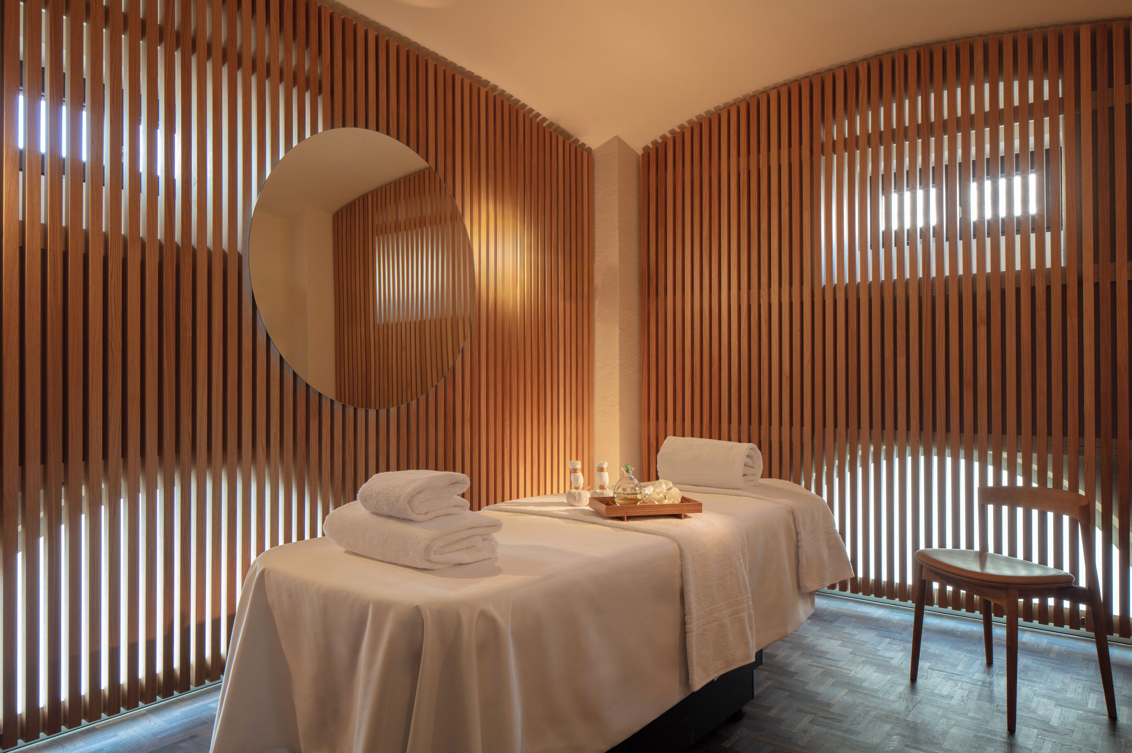 Un cuarto de spa con una cama, un sillón y una bandeja con detalles de cortesía.