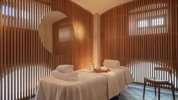 Un cuarto de spa con una cama, un sillón y una bandeja con detalles de cortesía.