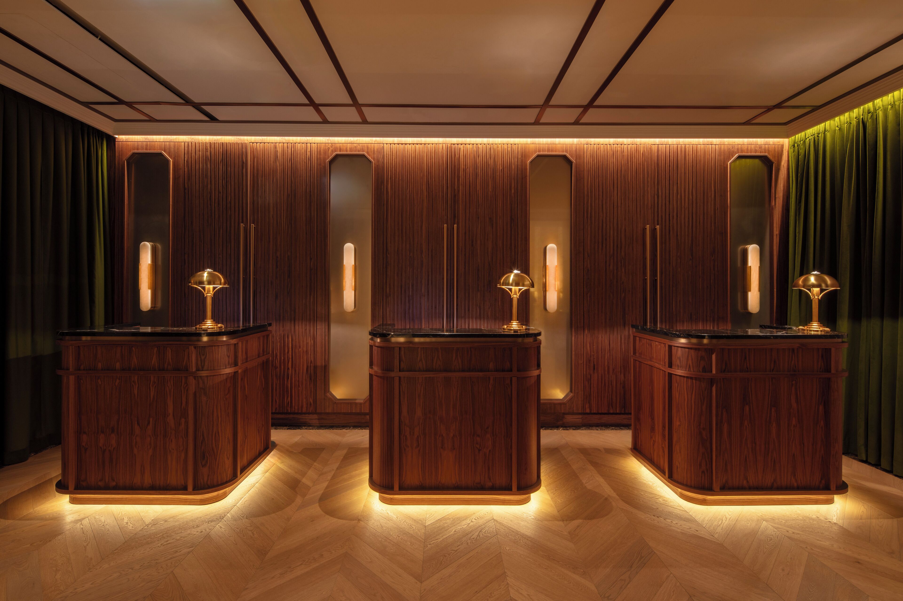 A hotel lobby with three wooden reception desks, a herringbone floor pattern, and a green curtain.