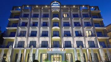 A multi-story hotel with a central entrance, balconies, and outdoor seating areas.