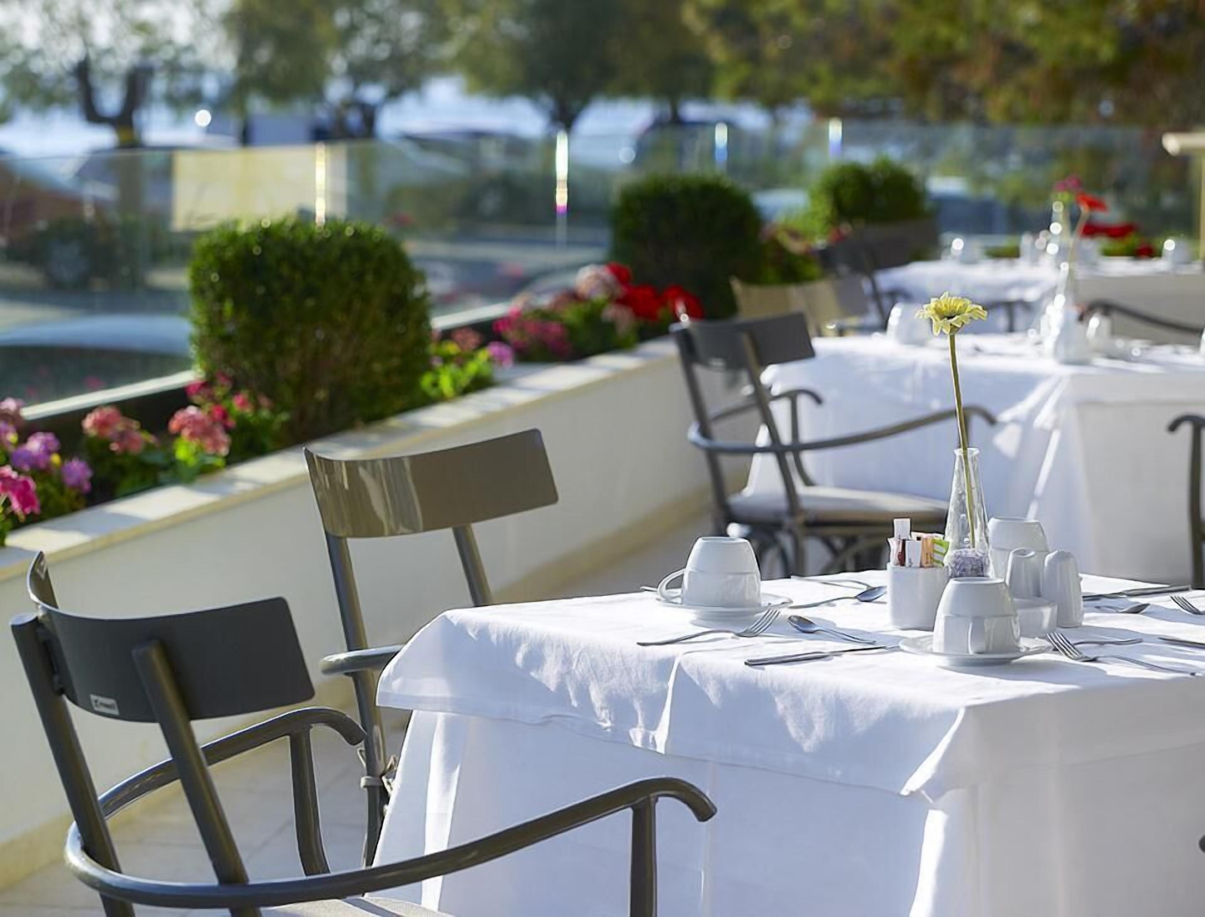 Un área de comedor al aire libre con mesas dispuestas para dos, sillas y un jarrón con una sola flor.