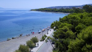 Una playa costera con gente nadando y tomando el sol, un paseo marítimo pavimentado y una carretera que lleva a la playa.