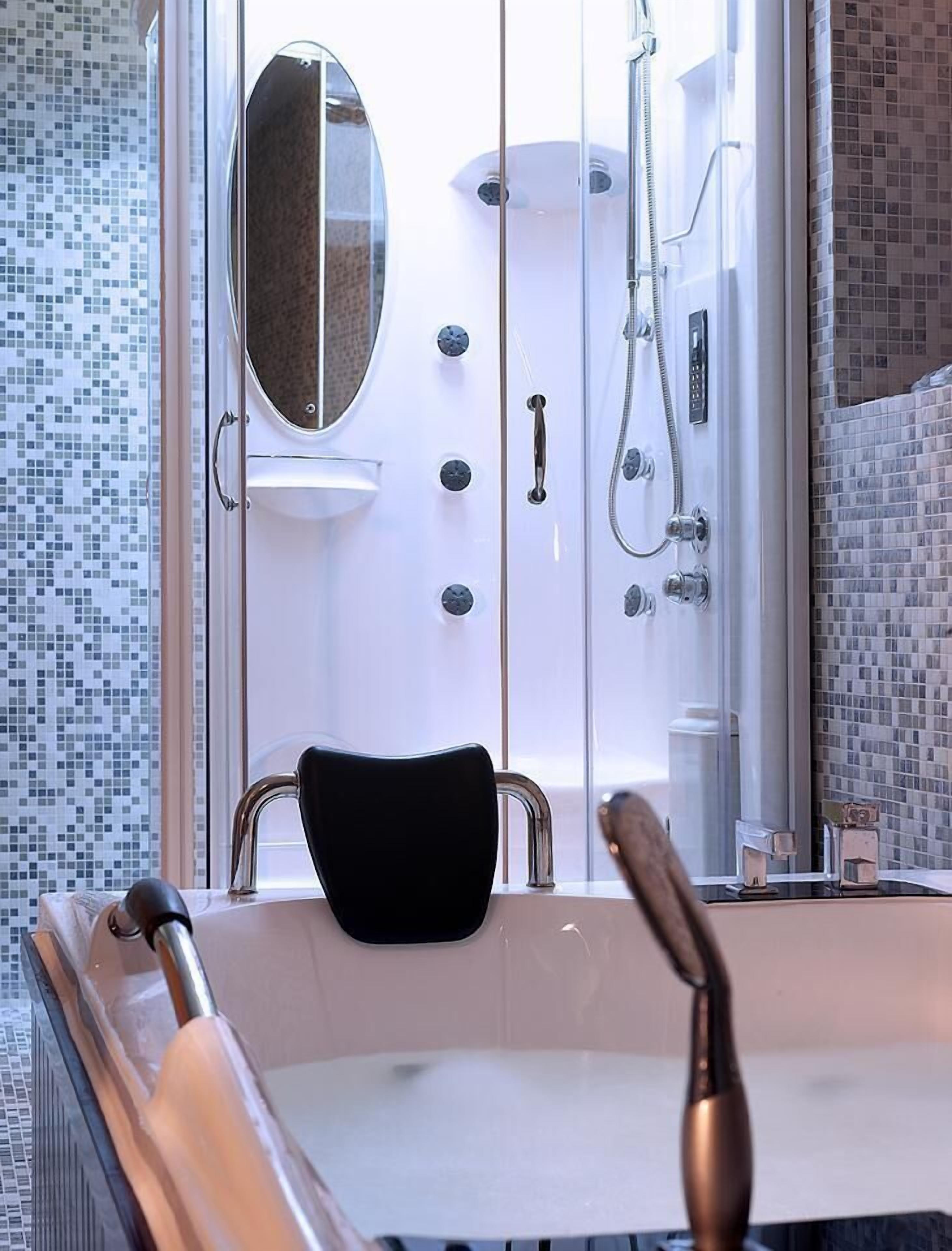 A modern bathroom with a glass-enclosed shower, a black chair, and a bathtub.