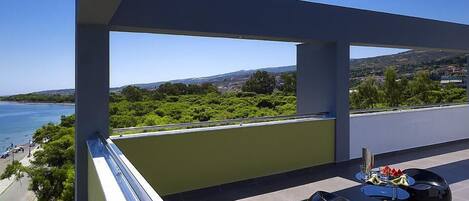 A balcony with a view of the sea, green landscape, and distant hills.