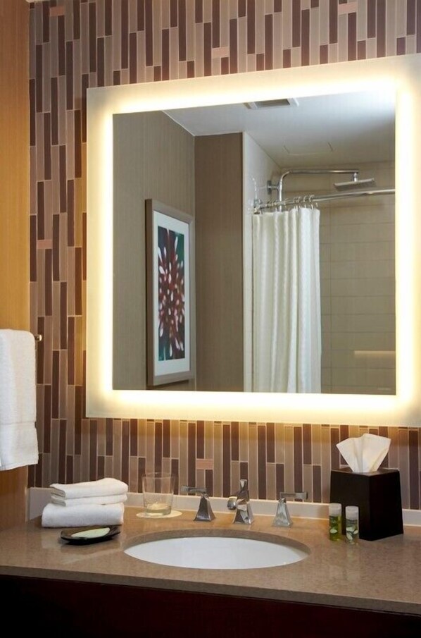 A bathroom with a large mirror, a sink, a towel rack, and a framed artwork on the wall.