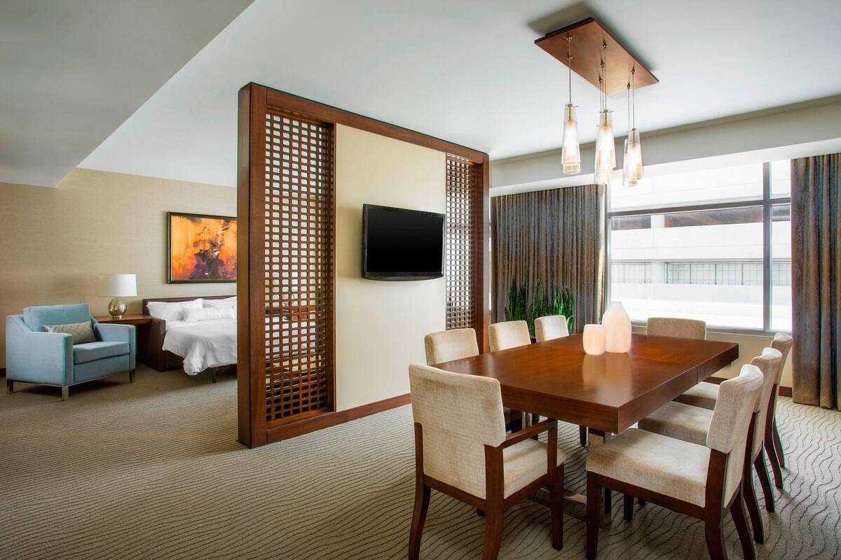 Habitación de hotel con comedor, televisión, sofá y ventana grande.