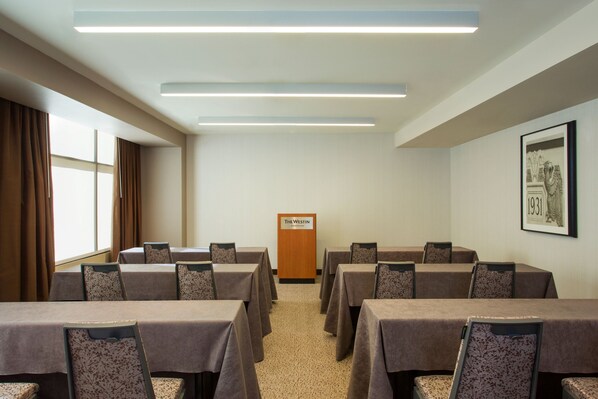 A conference room with tables and chairs, a podium, and a framed picture on the wall.