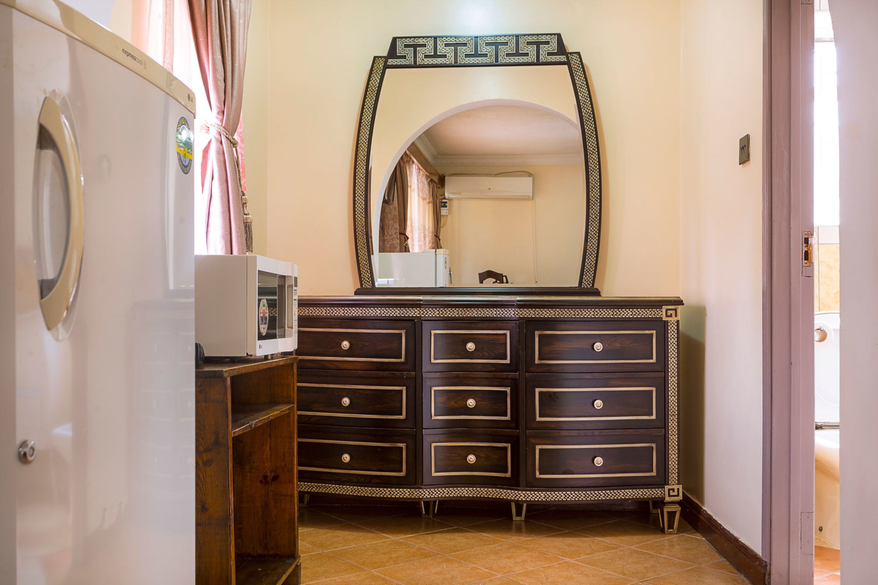 A compact room with a built-in wardrobe, a microwave, and a large mirror above the dresser.