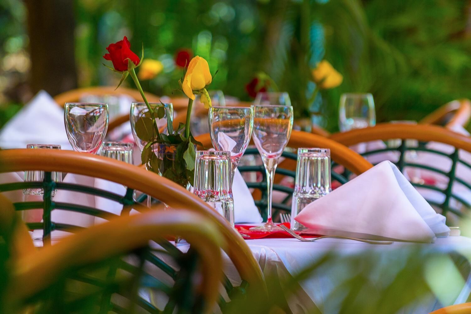Una mesa al aire libre con cristalería transparente y un florero con flores.