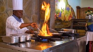 A chef performing a flambé with a pan on a stove in a kitchen.