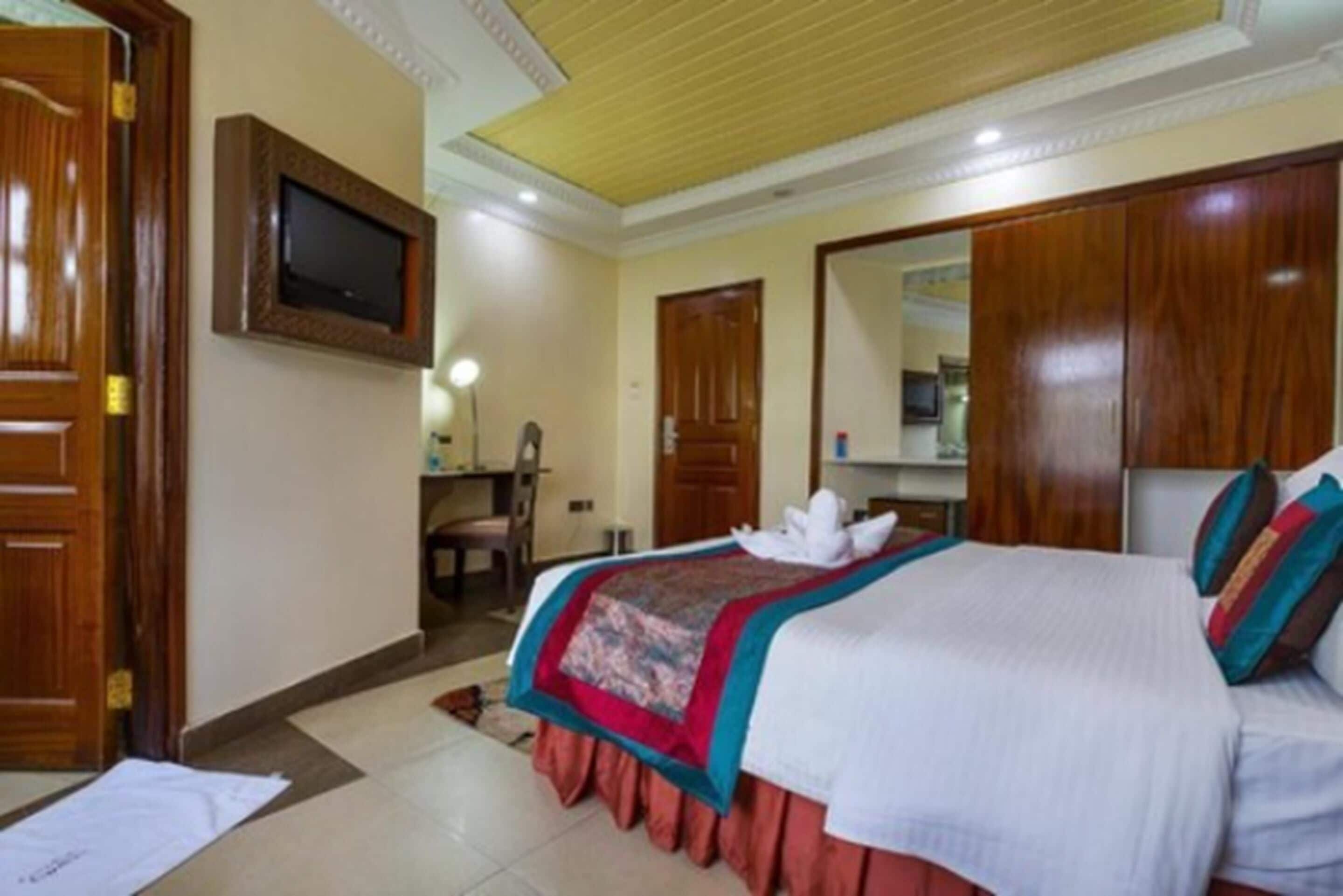 Une chambre d’hôtel comprenant un lit, un bureau avec une chaise, un téléviseur fixé au mur et une armoire.