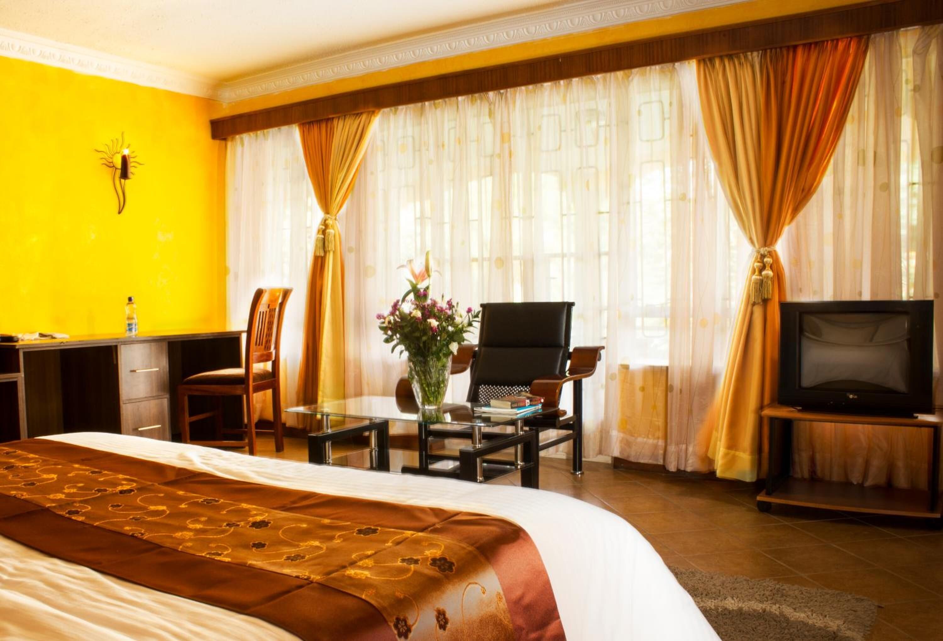 A hotel room with a large bed, a desk with a chair, a television, and curtains.