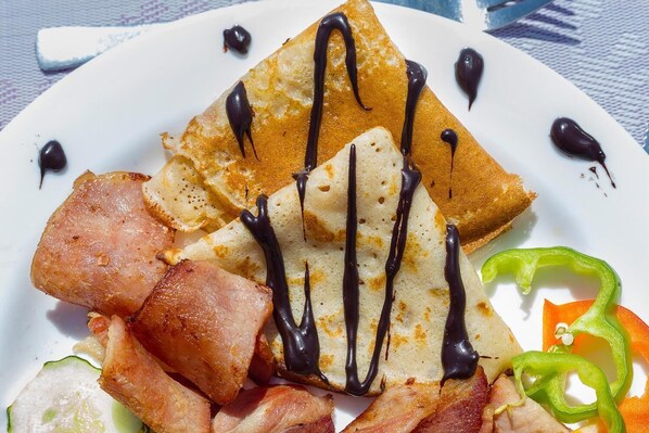 Ein Teller mit Pfannkuchen, Speck und einer grünen Paprika.