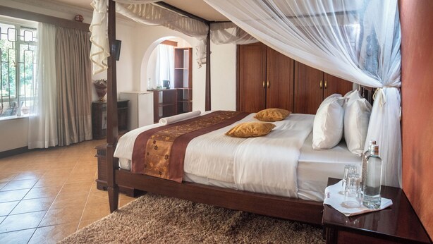 A four-poster bed with a canopy, a wooden wardrobe, and a small table with a bottle and glasses.
