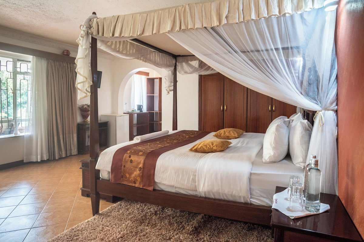 A four-poster bed with a canopy, a wooden wardrobe, and a small table with a bottle and glasses.