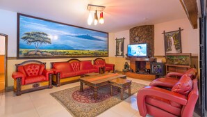 A living room with red leather sofas, a wooden coffee table, a large painting of a landscape, a television, and a fireplace.