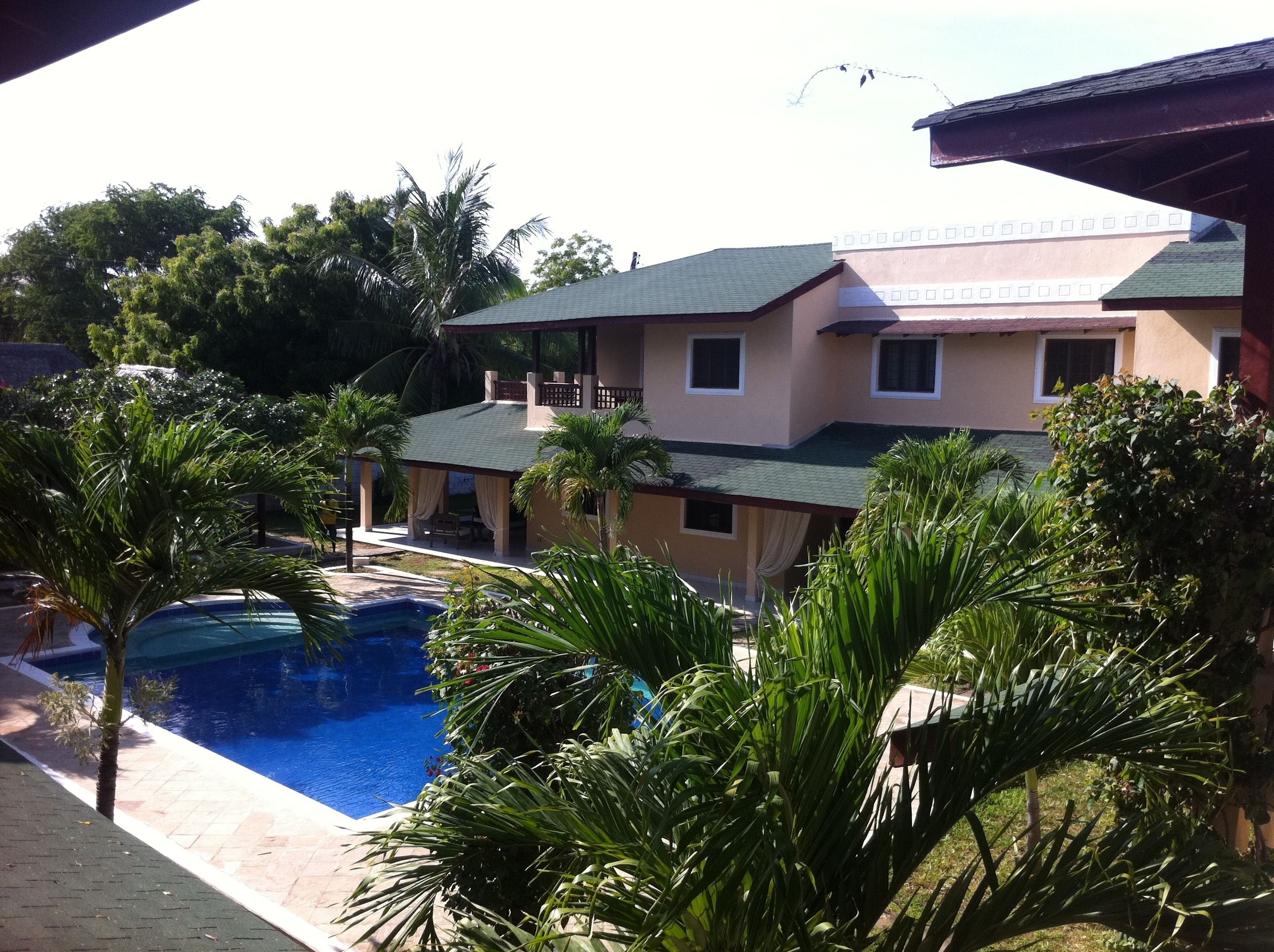 A two-story house with a swimming pool, surrounded by palm trees and greenery.