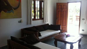 Una sala de estar con sofá, mesa de centro de madera, un cuadro en la pared y una ventana con cortinas.