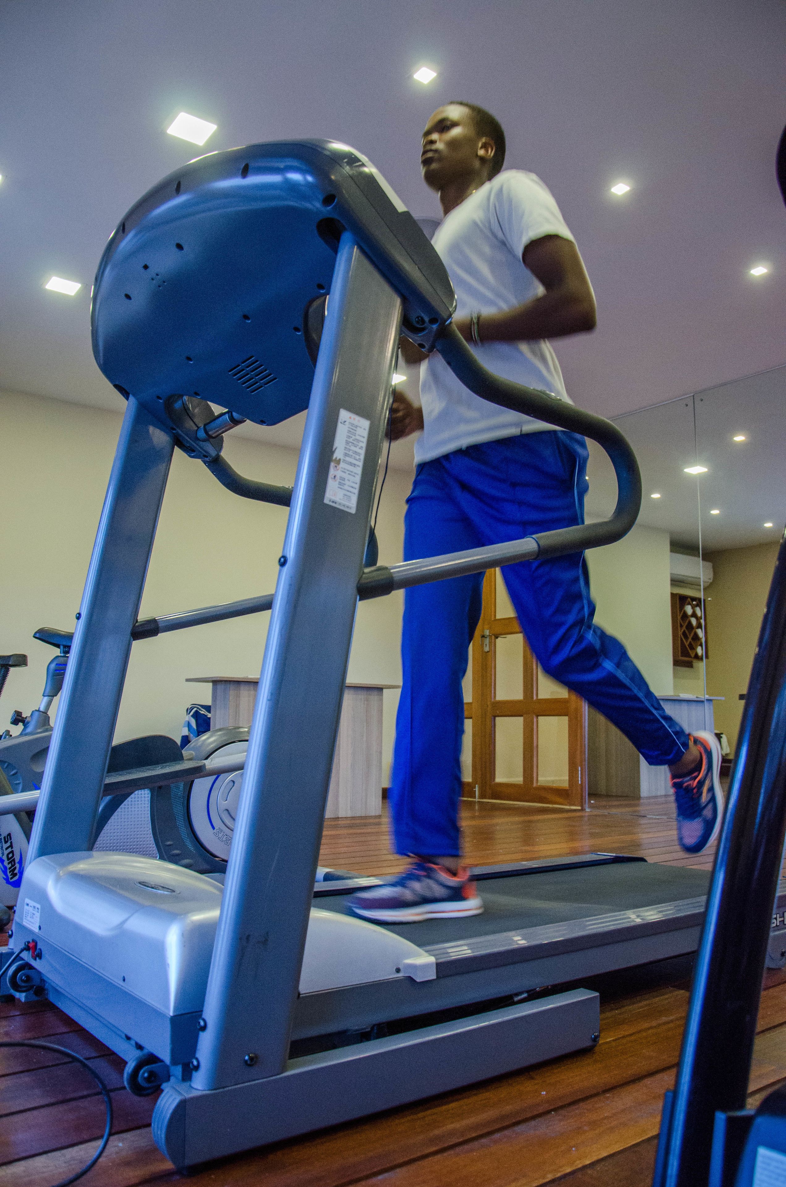 Una persona corriendo en una cinta de correr dentro de un gimnasio con equipo de ejercicio y un espejo en la pared.