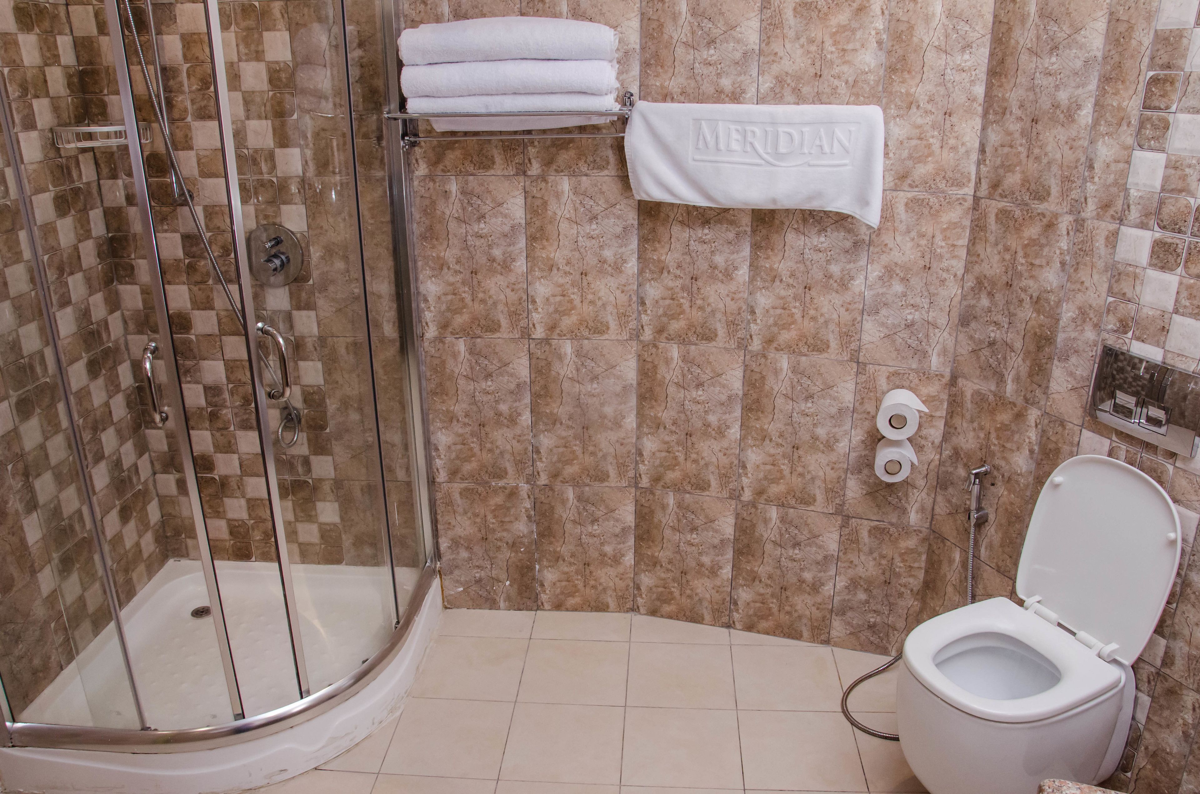 Un baño con ducha de vidrio, inodoro y perchero con una toalla que dice "MERIDIAN".