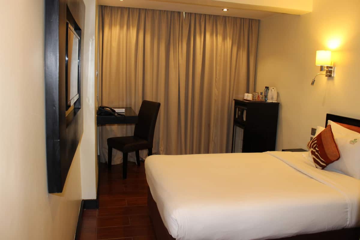 Une chambre d’hôtel avec un lit, un bureau, une chaise et une armoire.