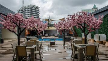 An outdoor seating area with tables and chairs, a pool, and cherry blossom trees.