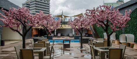 An outdoor seating area with tables and chairs, a pool, and cherry blossom trees.