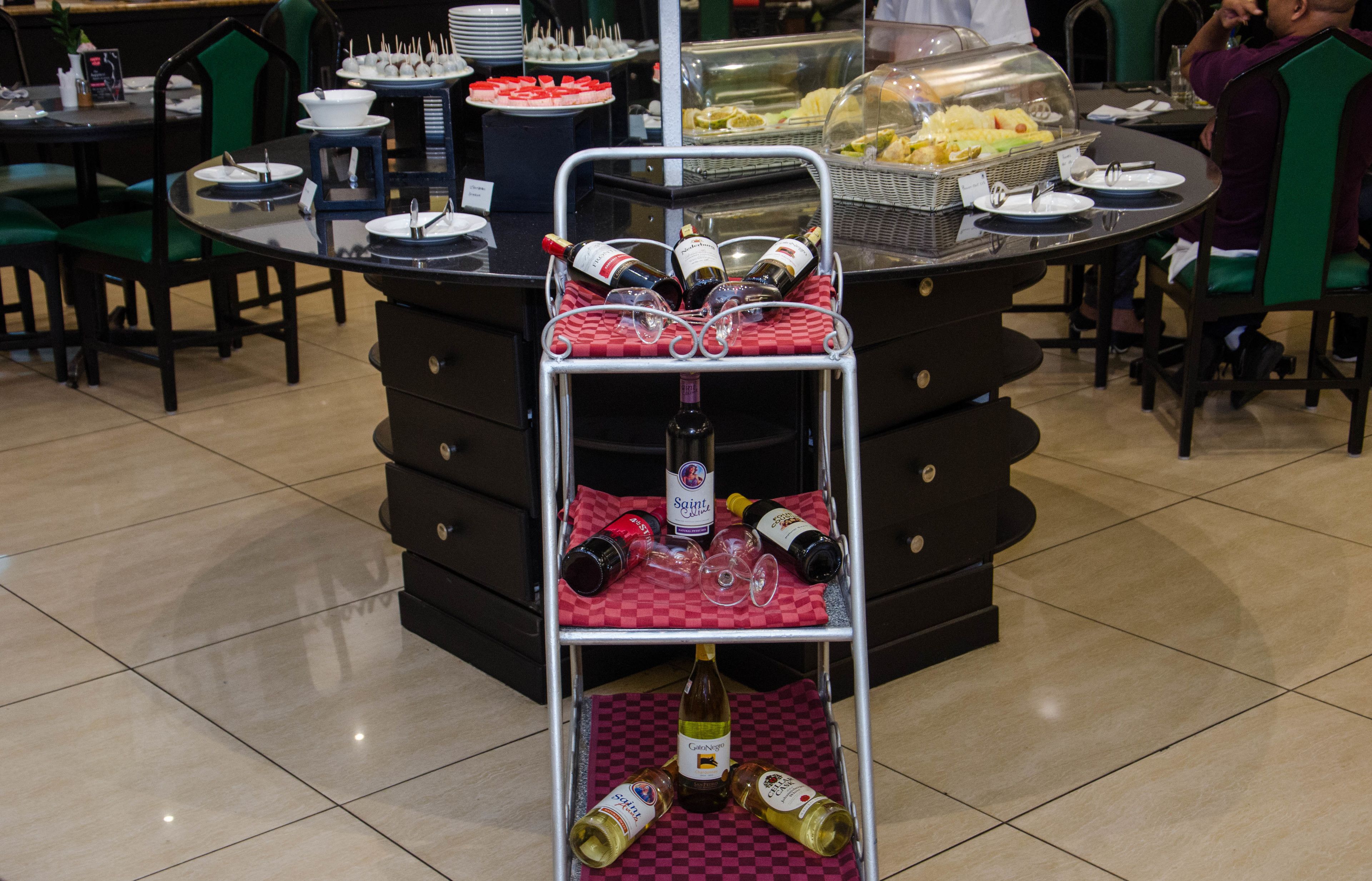 A buffet setup with a wine cart, plates, and various food items.