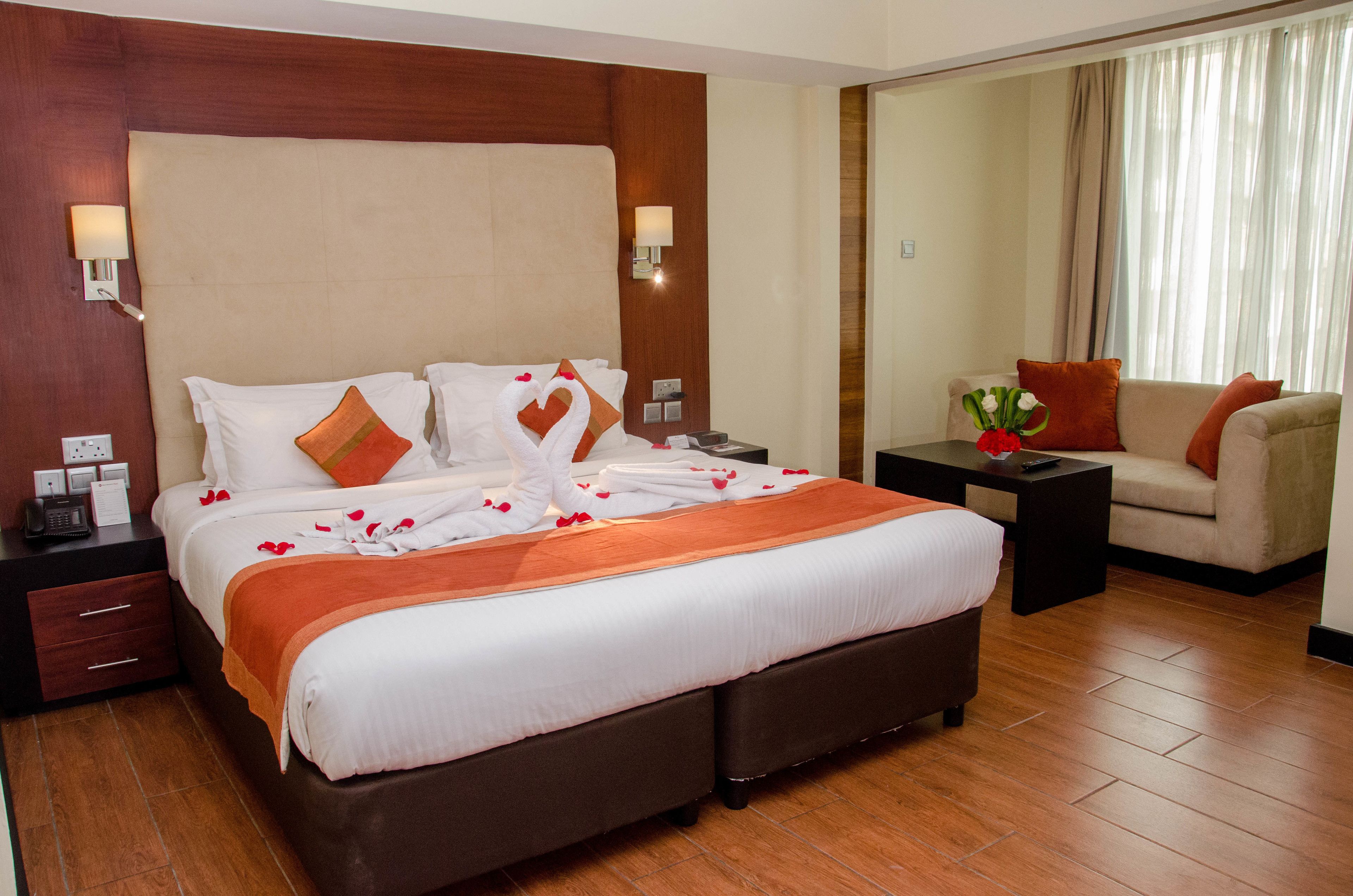 Een hotelkamer met een groot bed, twee nachtkastjes, een salontje en een spiegel.