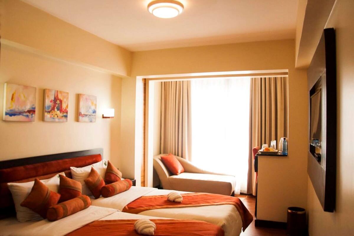 Une chambre d’hôtel avec deux lits, un coin salon et une grande fenêtre avec des rideaux.