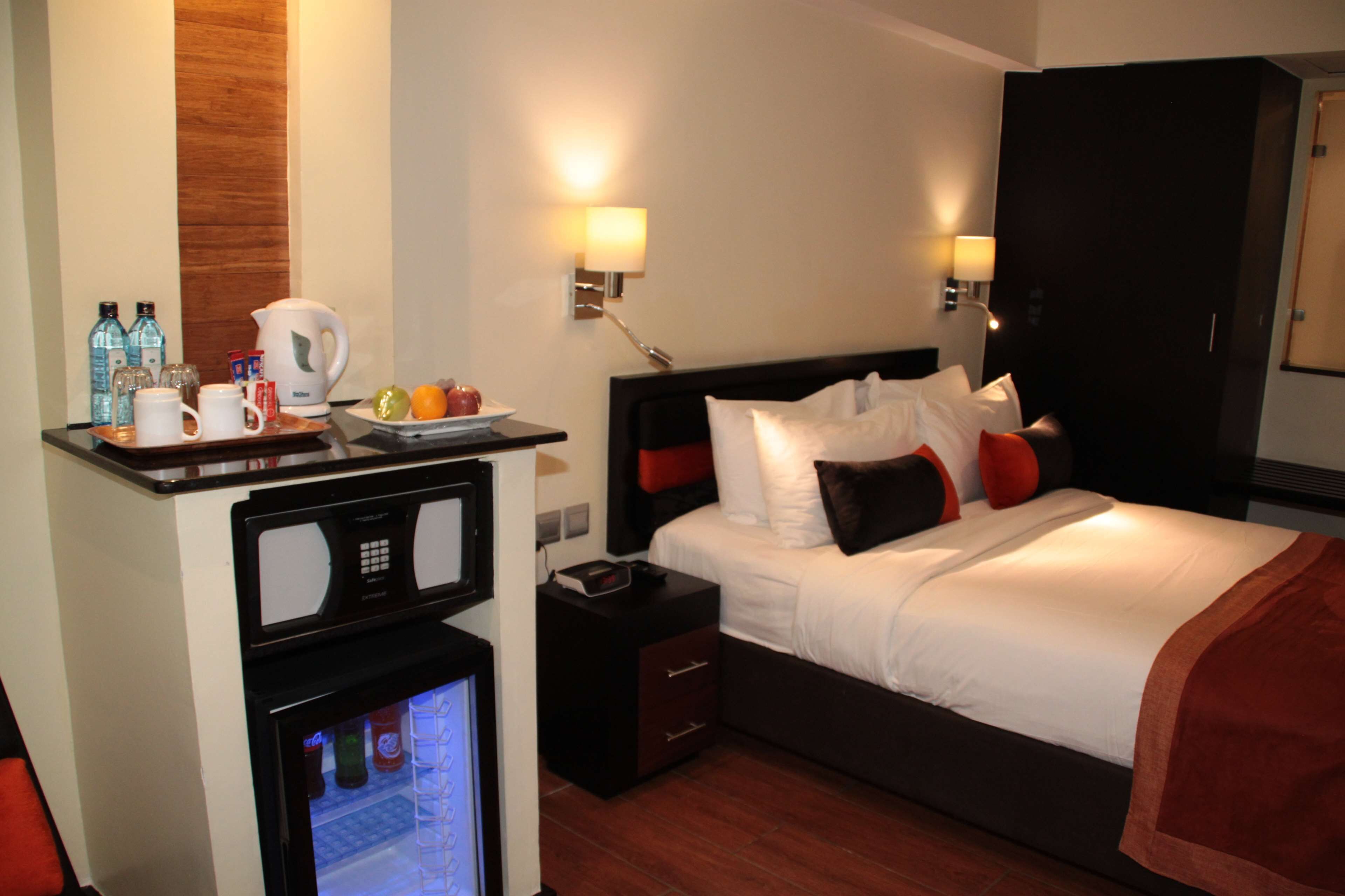 A hotel room with a bed, bedside tables, a minibar, and a wall-mounted TV.