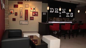 Una zona de bar con sillas rojas, una barra con botellas y cuadros en la pared.